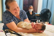 A smiling woman holds a newborn.