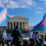 People carrying transgender pride flags and other signs stand outside the Supreme Court building.