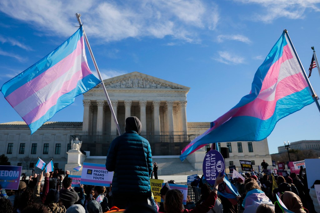 People carrying transgender pride flags and other signs stand outside the Supreme Court building.