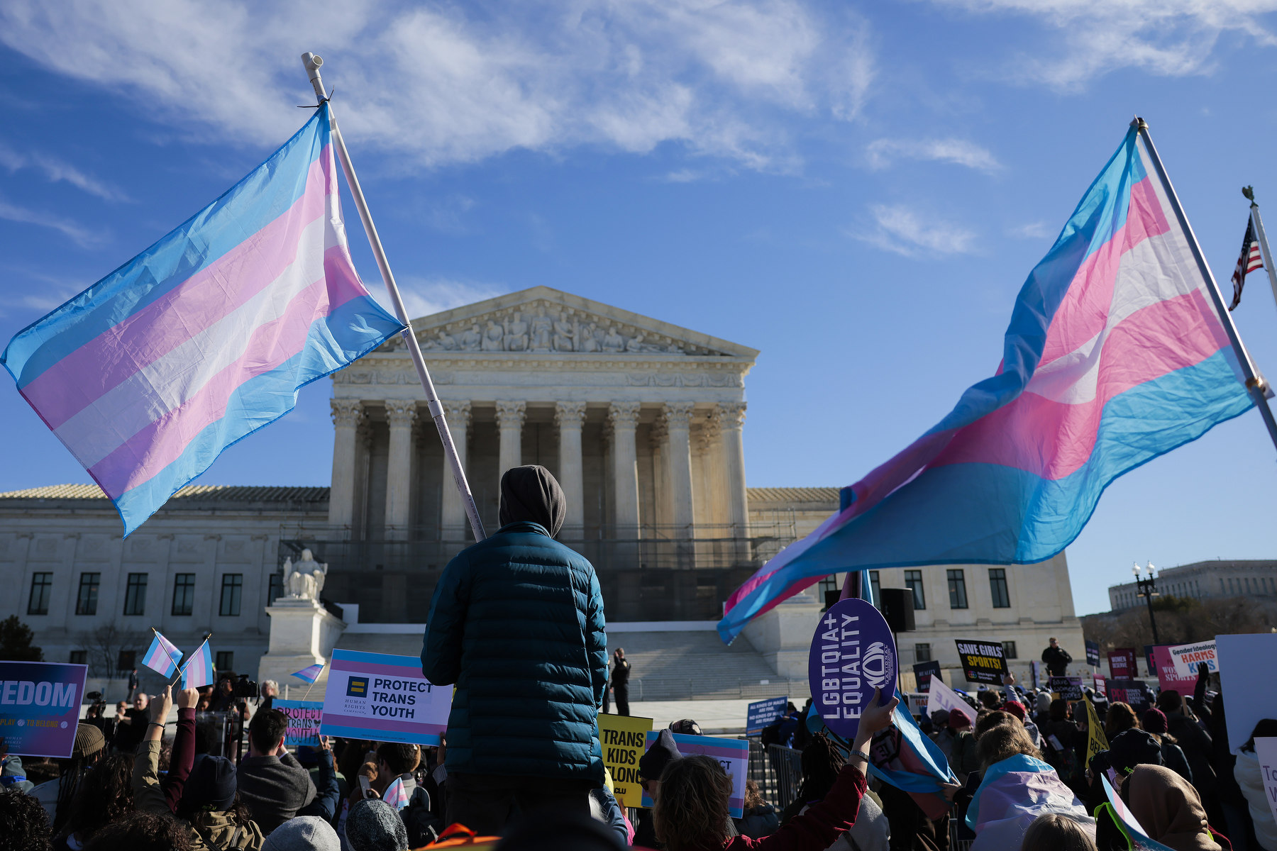 People carrying transgender pride flags and other signs stand outside the Supreme Court building.