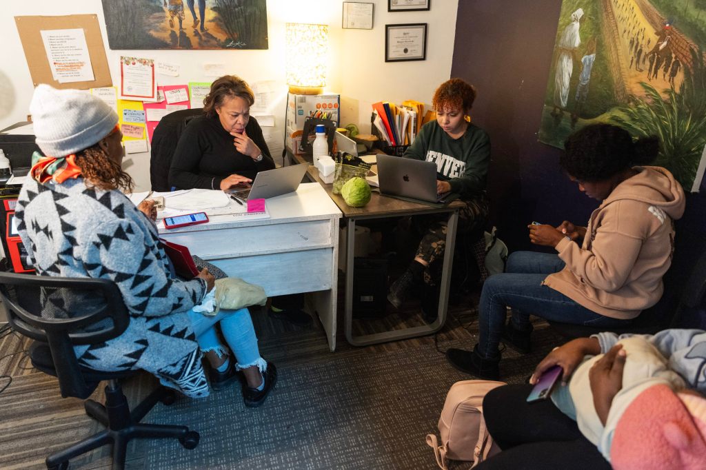 Five people sit in a small office, one holding a baby.