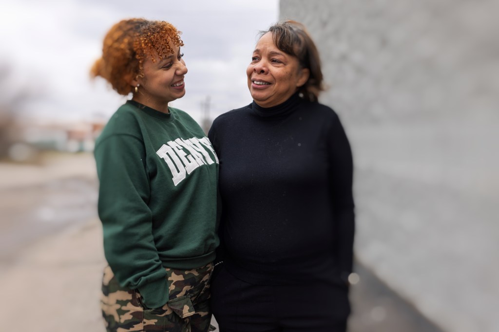 Mother and daughter smile at each other while standing outside.