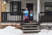 Two children hold protest signs on a front stoop surrounded by snow.