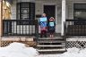 Two children hold protest signs on a front stoop surrounded by snow.