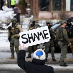 An onlooker holds a sign that reads “Shame” as members of law enforcement work the scene following the fatal shooting of Renee Nicole Good by an ICE agent.