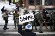 An onlooker holds a sign that reads “Shame” as members of law enforcement work the scene following the fatal shooting of Renee Nicole Good by an ICE agent.