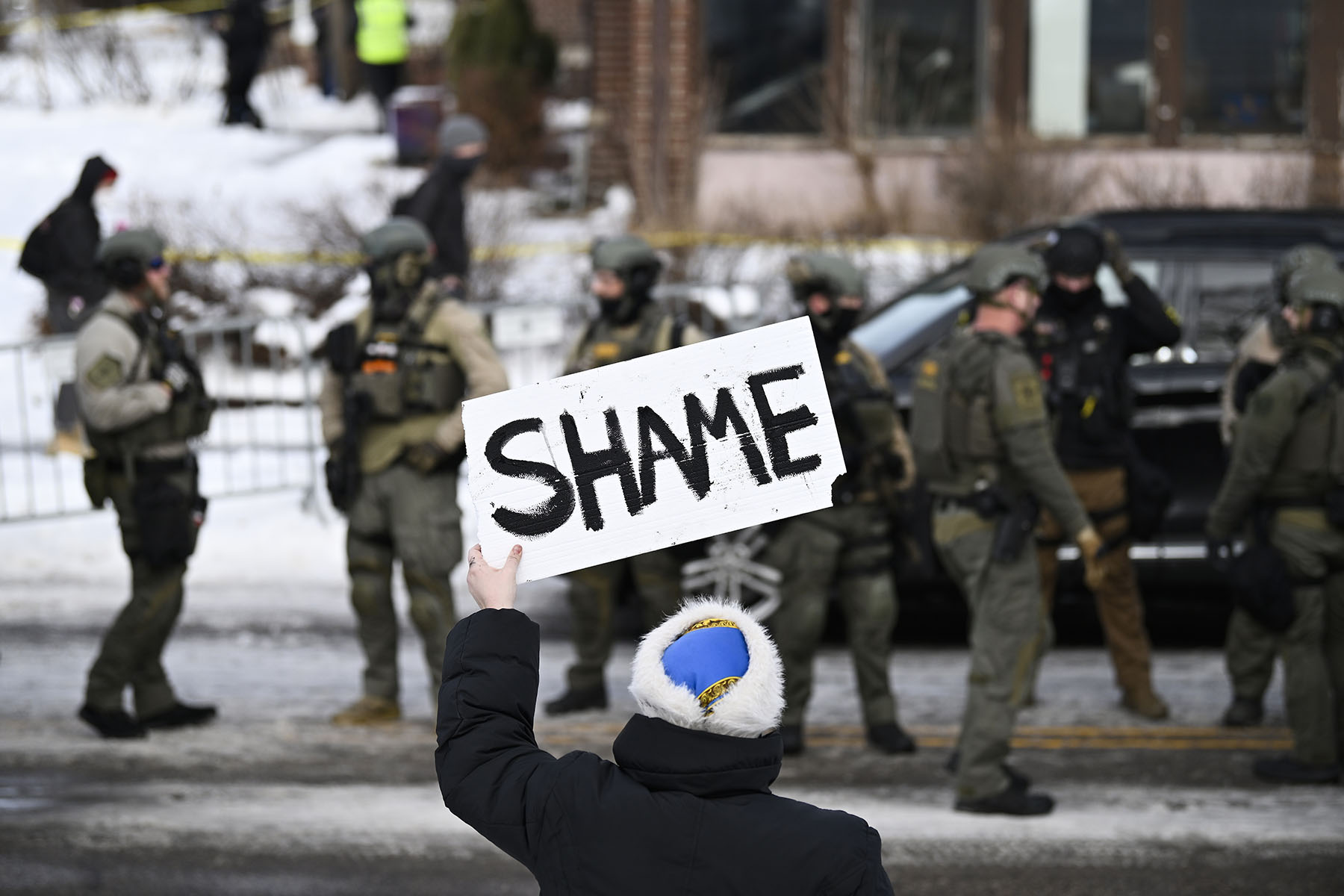 An onlooker holds a sign that reads “Shame” as members of law enforcement work the scene following the fatal shooting of Renee Nicole Good by an ICE agent.