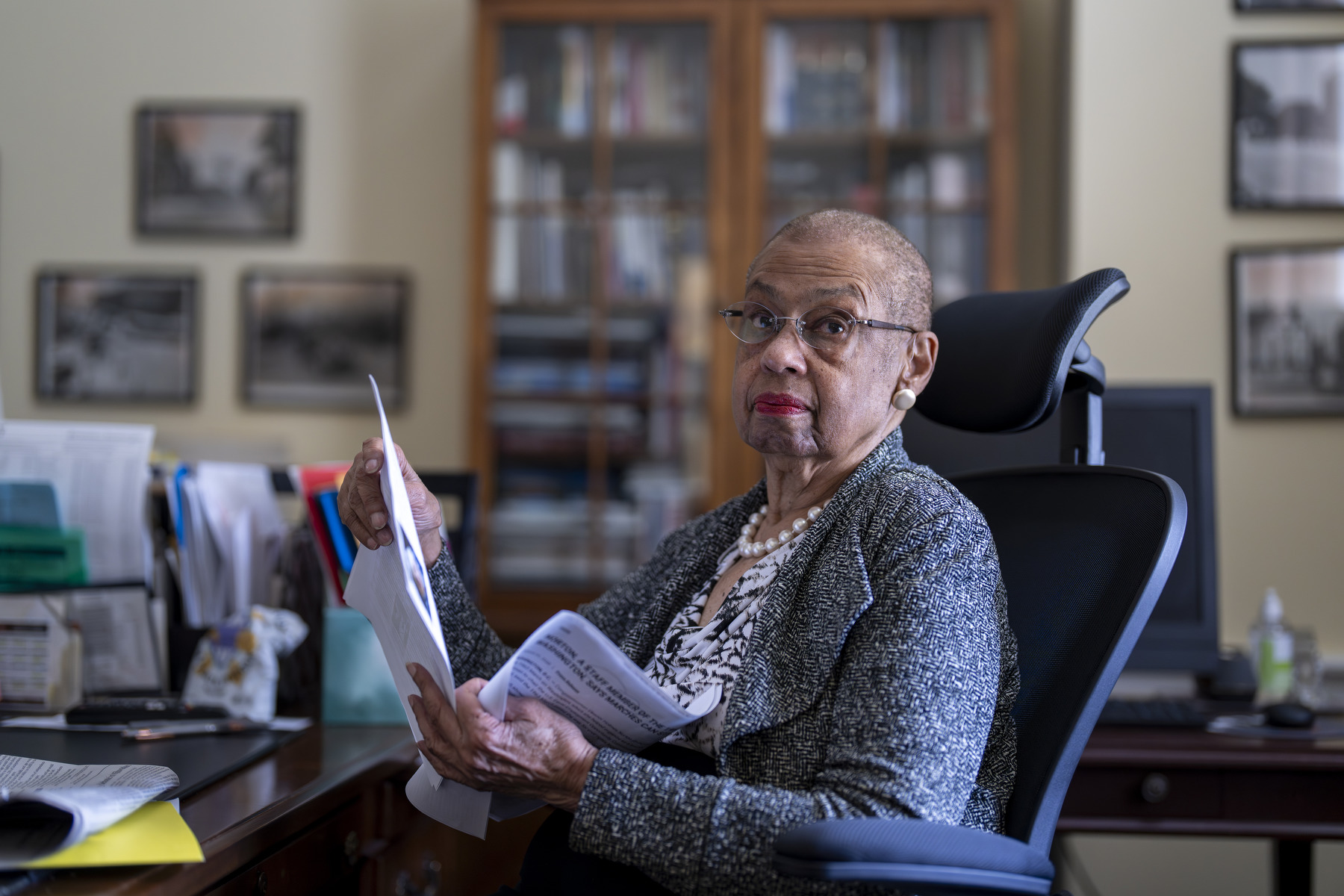 Norton sits in a chair in an office holding papers as she looks toward the camera.
