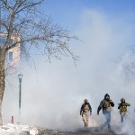 Masked ICE agents walk through tear gas on a street in Minneapolis.