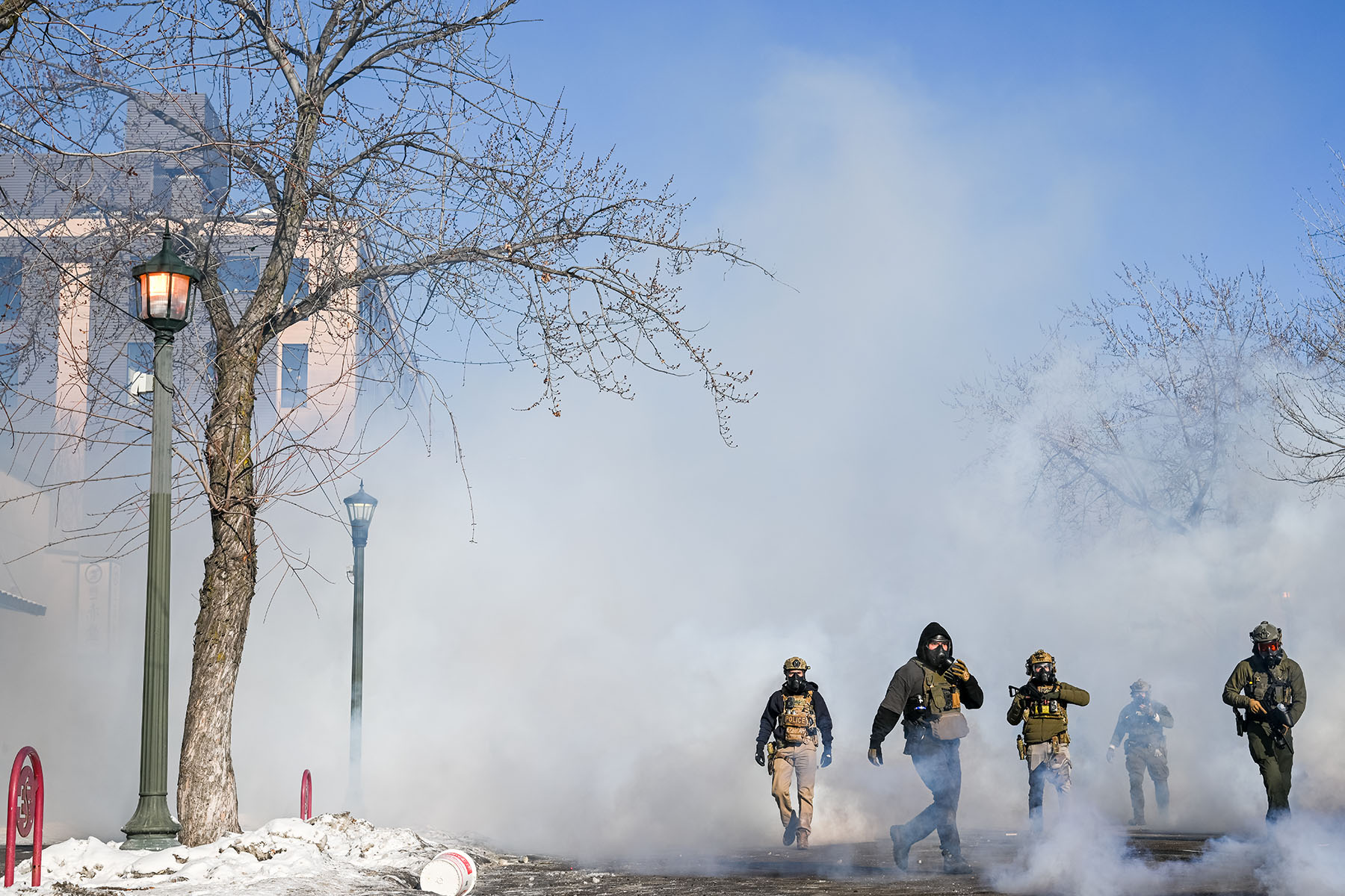 Masked ICE agents walk through tear gas on a street in Minneapolis.