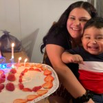A woman holds a child smiling by a cake with candles.