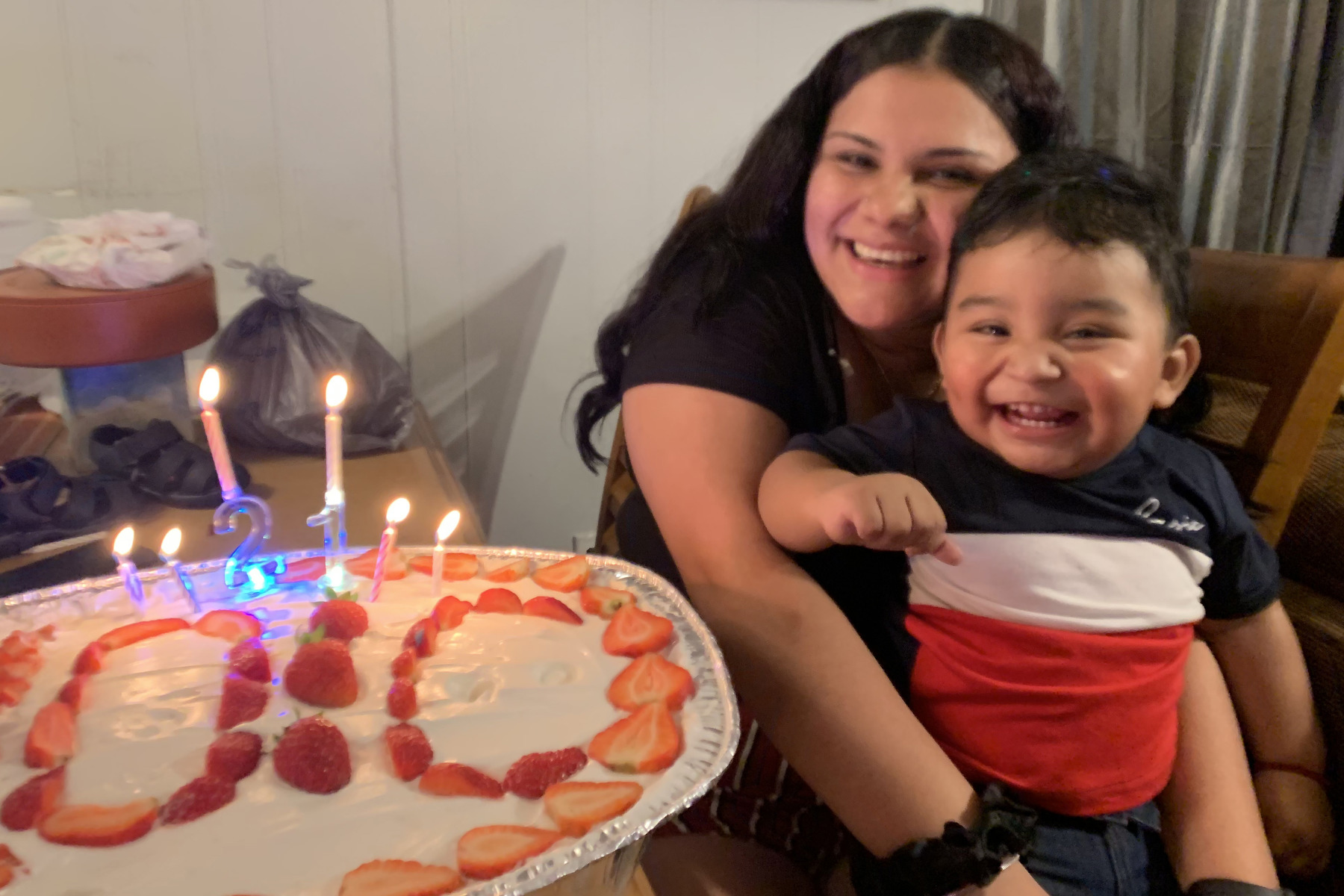 A woman holds a child smiling by a cake with candles.