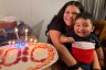 A woman holds a child smiling by a cake with candles.