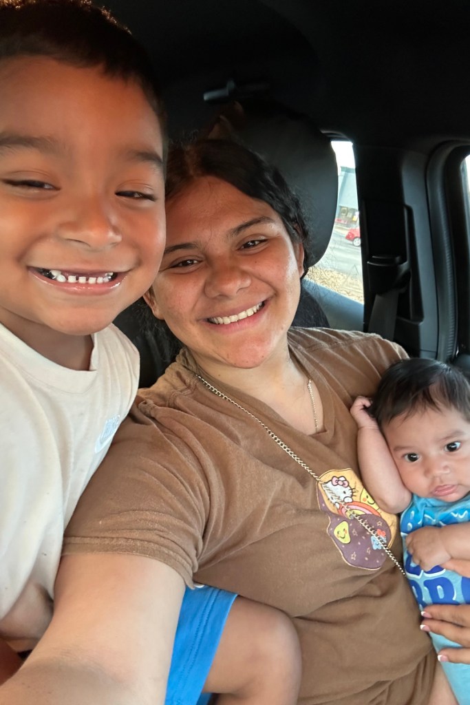A smiling mother holds a baby beside another child.