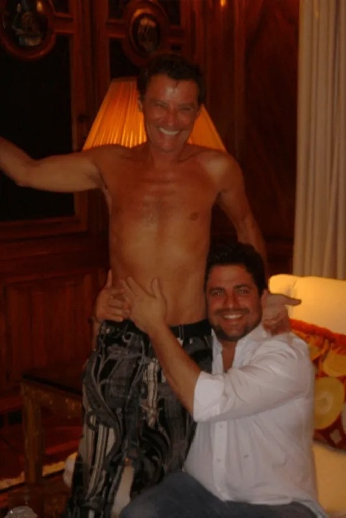 Two men embrace, one of them shirtless.