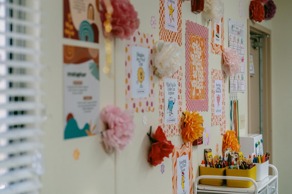 A wall of craft flowers and brightly colored posters in a classroom.