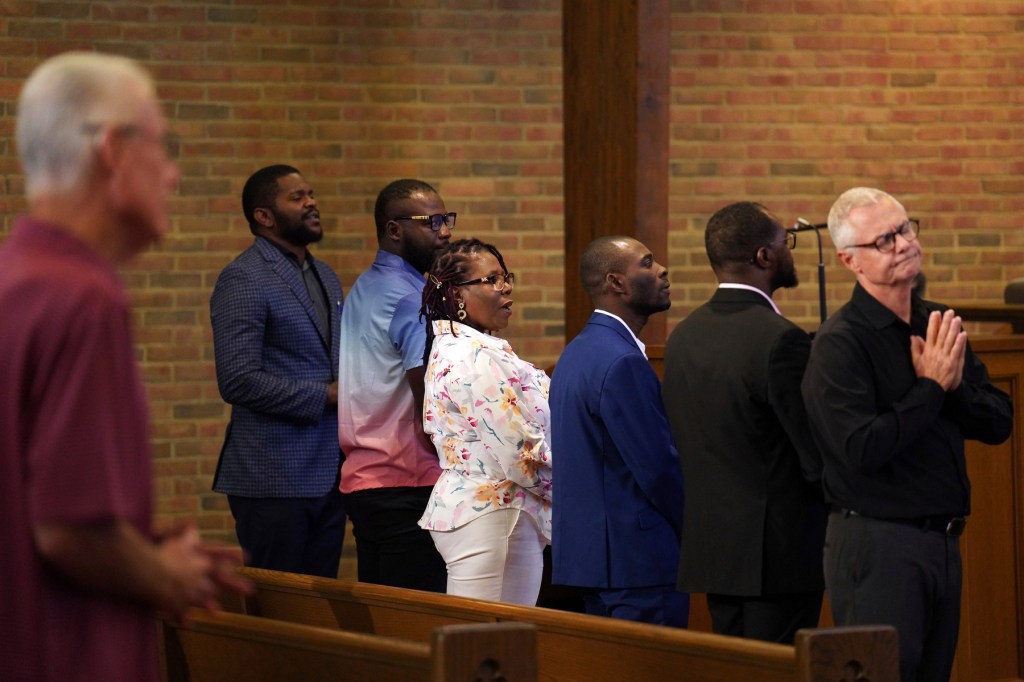 A line of congregants stand in a pew at a church.