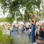 Dr. Annie Andrews speaks into a microphone at an outdoor campaign event, standing before a large crowd holding signs.