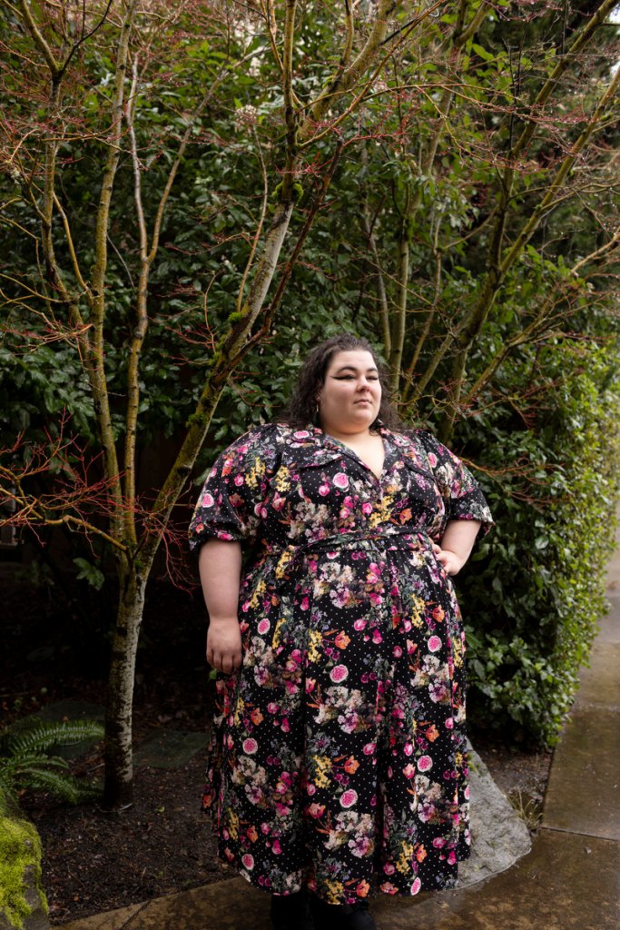 A portrait of a woman in a colorful floral dress surrounded by greenery.