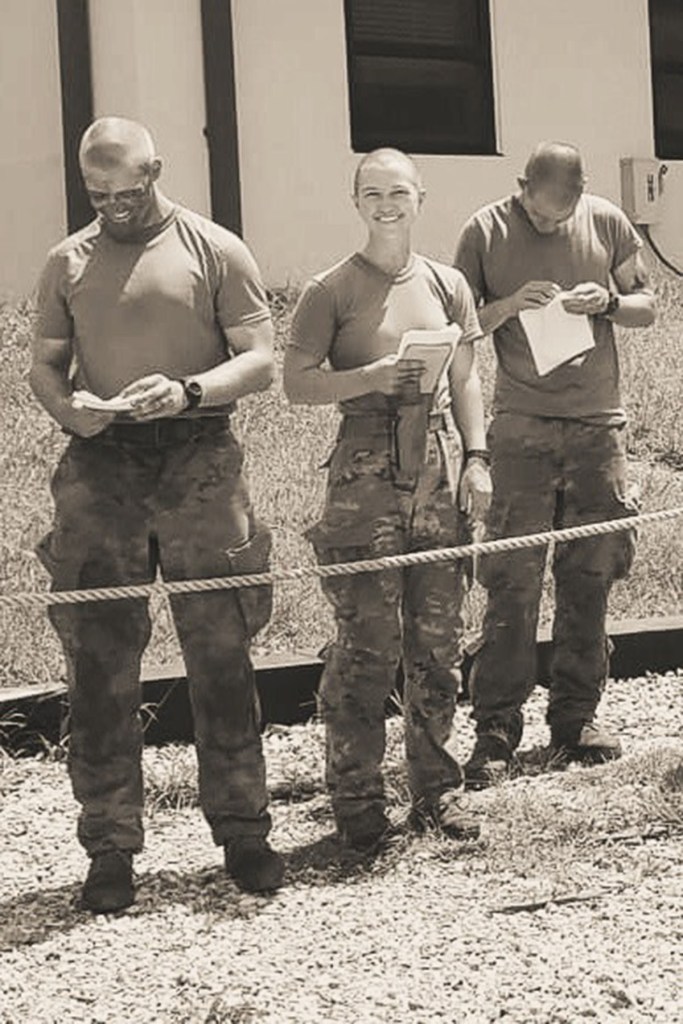 Mikayla Blaska stands alongside two fellow soldiers during training, holding a notebook while wearing a short-sleeve Army uniform.