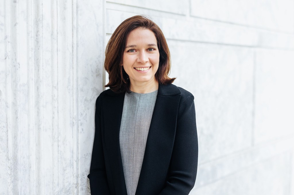 Rebecca Bennett smiles in a portrait, standing near a light-colored stone wall and wearing a dark blazer.