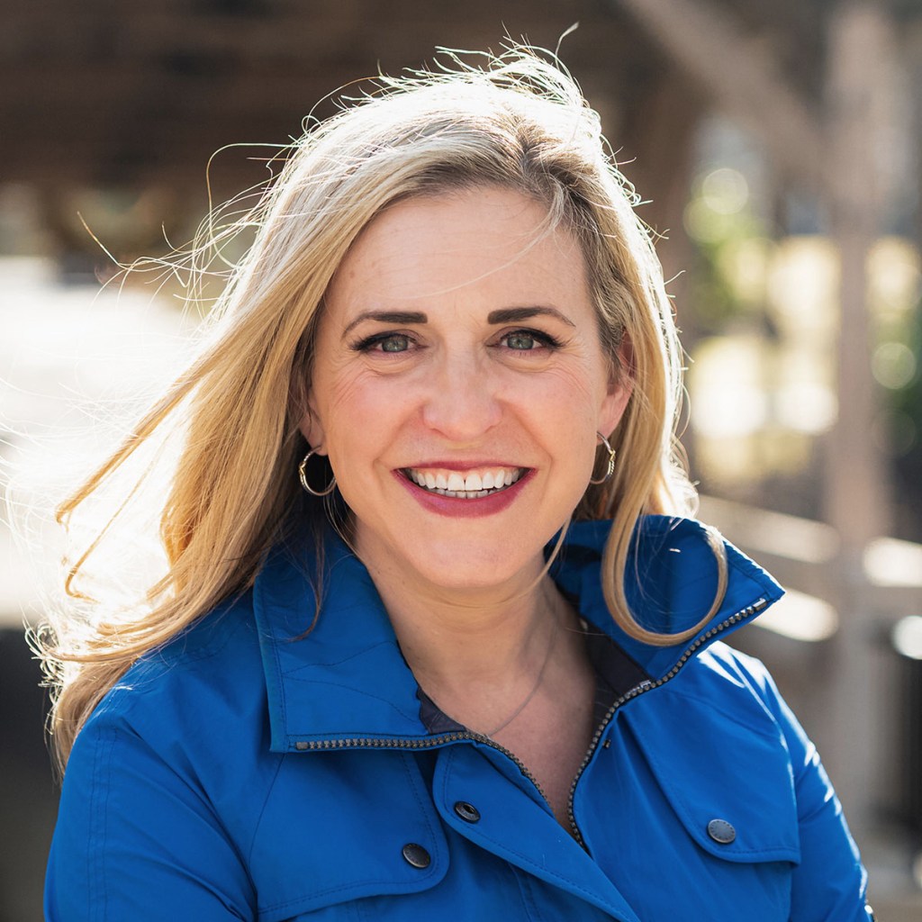 Maura Sullivan smiles in an outdoor portrait wearing a blue jacket.
