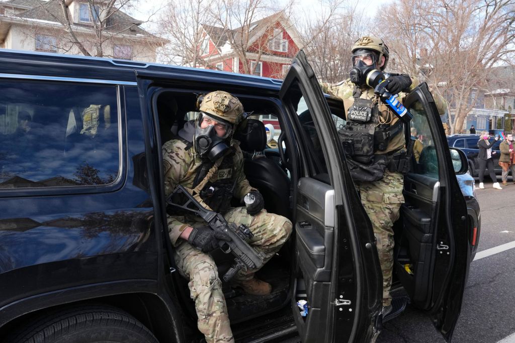 Federal agents wear gas masks and hold canisters while leaving out of a vehicle.