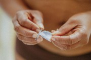 Mid section of woman holding hormone patch in front of belly.