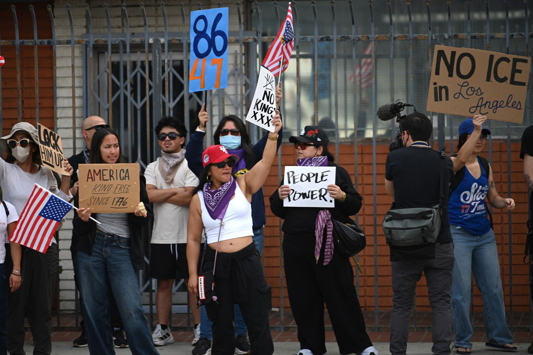 A group of people carrying signs and U.S. flags stand along a wall.
