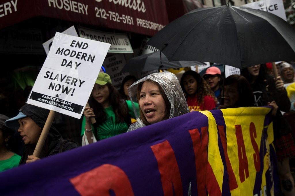 Filipina women walk down the street carrying signs, flags and umbrellas.