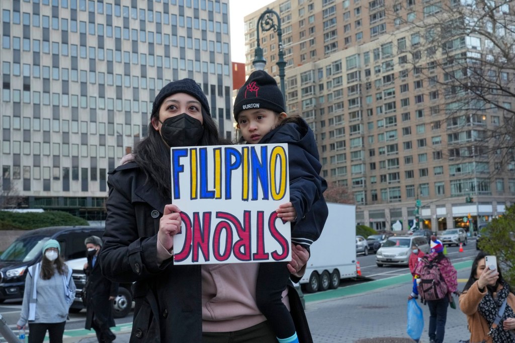A woman holds a child in her arms and a sign that says"Filipino Strong"