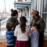 A family of five stand together on a patio facing away from the camera.