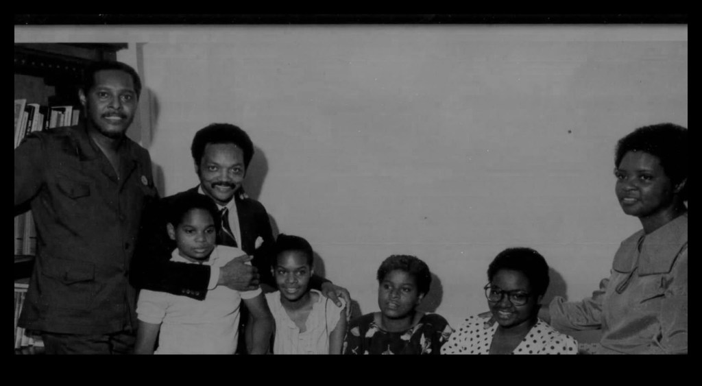 Black-and-white photo of the Rev. Jesse Jackson standing with Leah Daughtry’s family.