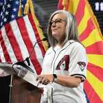 Katie Hobbs, in a Diamondbacks jersey, stands in front of Arizona and U.S. flags.
