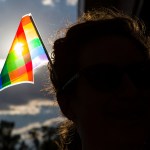 A silhouetted person wears a pride flag in their hair outdoors.
