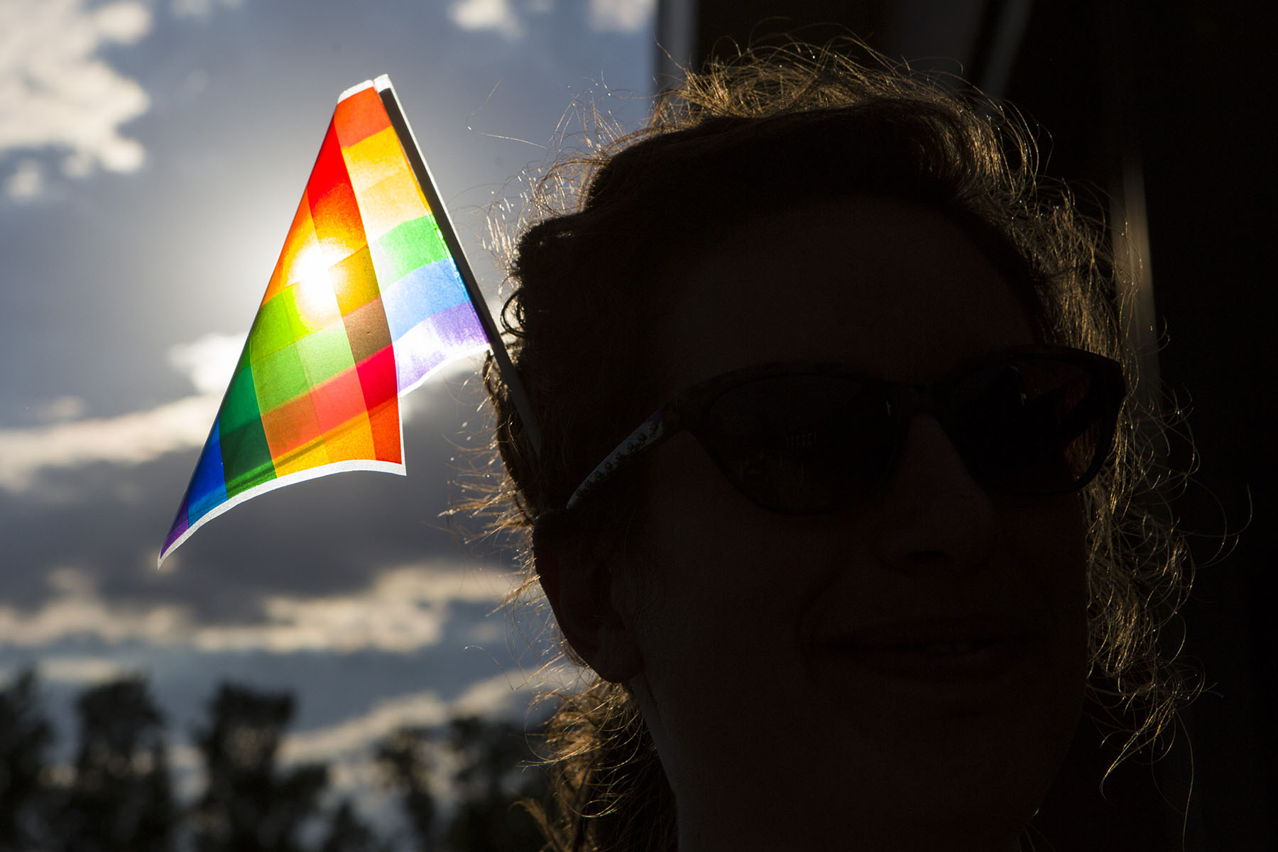 A silhouetted person wears a pride flag in their hair outdoors.