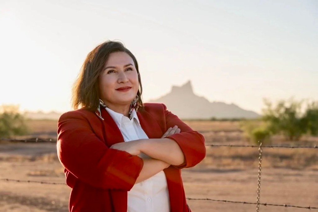 JoAnna Mendoza stands outdoors with her arms crossed, wearing a red blazer over a white shirt.