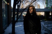 A portrait of Katie Paris standing on a wintery street, her face half in shadow.