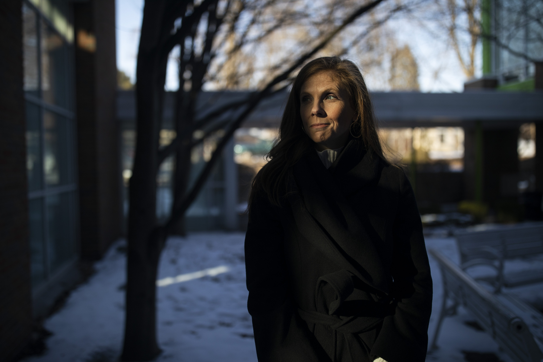 A portrait of Katie Paris standing on a wintery street, her face half in shadow.
