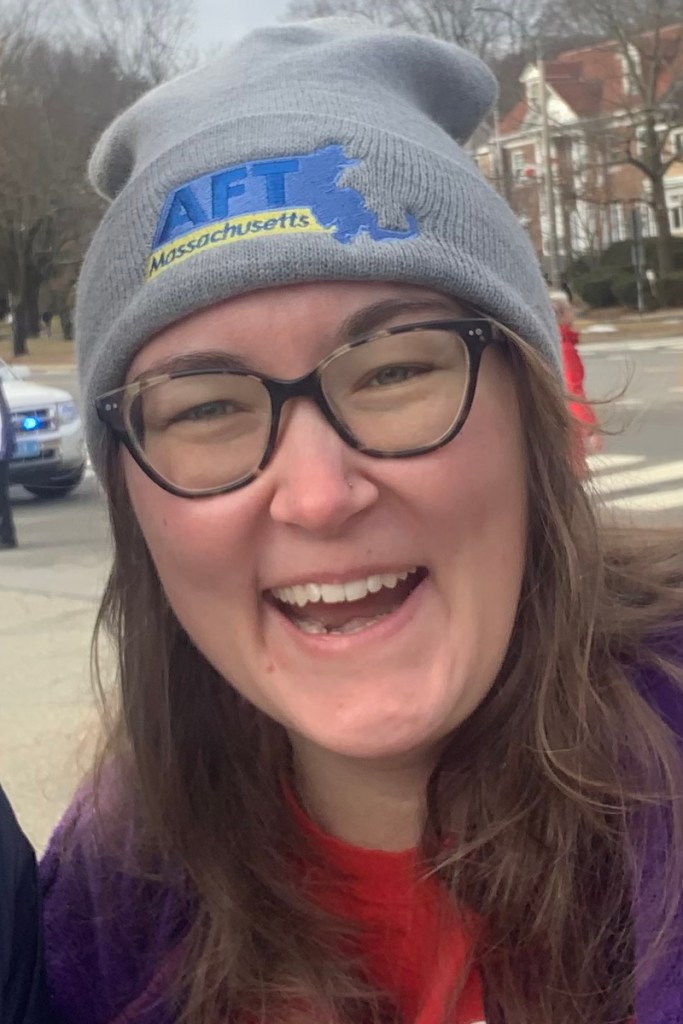 A closeup photo of a woman smiling wearing glasses and a hat that says AFT.