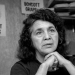 Huerta clasps her hands together in front of signs that say Boycott Grapes.