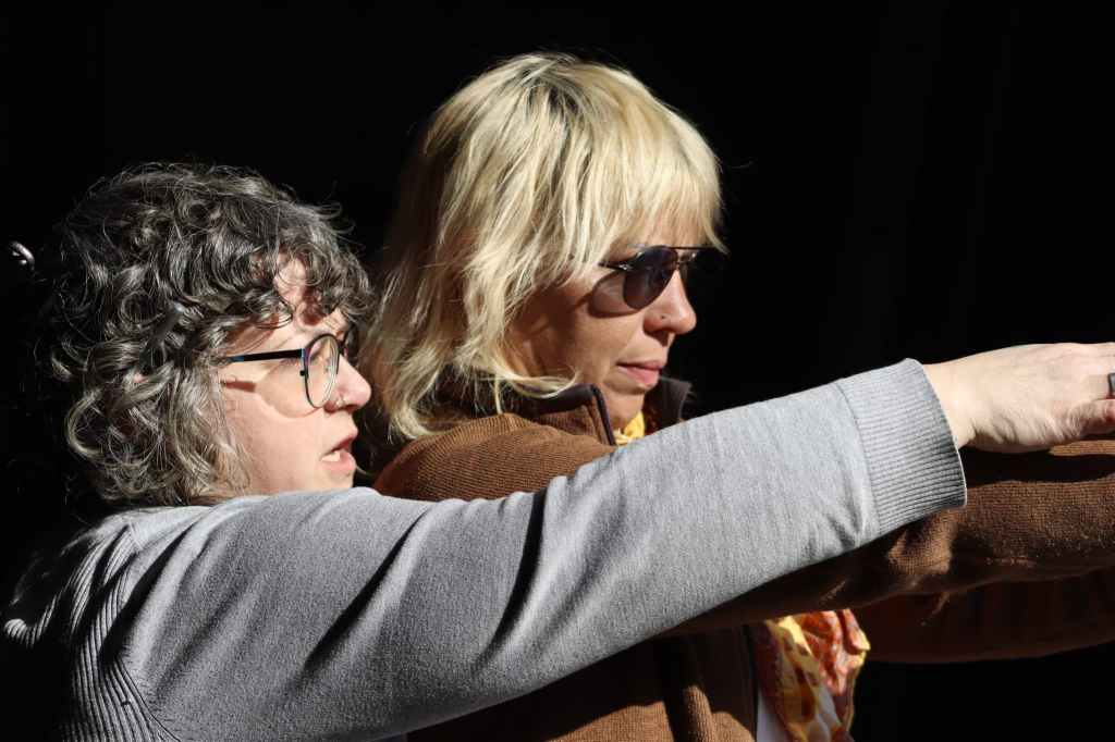 Two people stand side by side aiming handguns, concentrating on a target outside the frame.