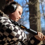 A person wearing hearing protection loads shells into a shotgun while standing outdoors.