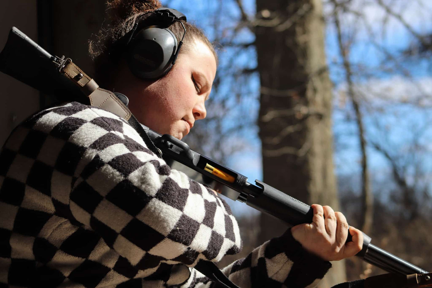 A person wearing hearing protection loads shells into a shotgun while standing outdoors.