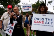 A group of people walk outdoors holding protest signs, including one that reads “Demand Only Citizens Vote” and another that says “Pass the SAVE Act - Protect Our Elections.”