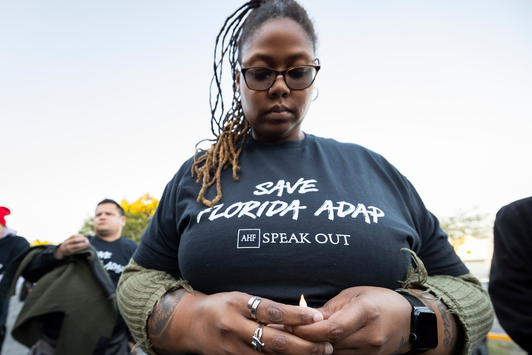 A woman wears a Save Florida ADAP t-shirt with her head bowed.