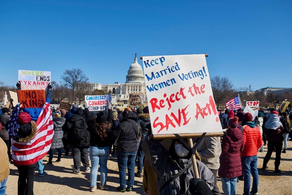 A crowd of protesters gathers on the National Mall in Washington, D.C., with the U.S. Capitol visible in the background. In the foreground, a large handmade sign reads “Keep Married Women Voting! Reject the SAVE Act!”