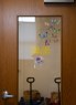 A glass door with butterfly stickers and the reversed text “ALL ARE WELCOME,” with carts visible inside the room beyond.