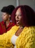 A close-up of a woman with curly red hair speaking, with another woman slightly out of focus beside her.