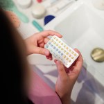 A woman holds a pack of birth control pills over the sink.